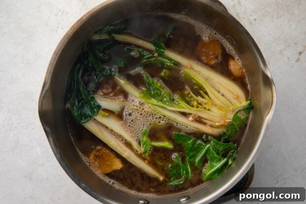 Ramen broth and bok choy in a silver pot