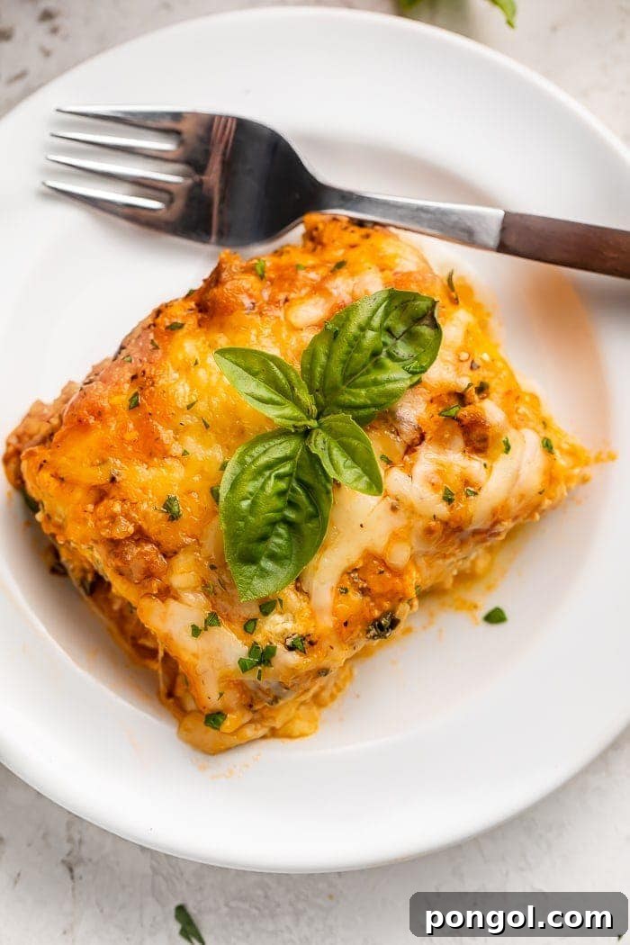 The Keto Lasagna Revelation 2 A perfectly sliced portion of delicious keto lasagna served on a white plate with a fork, ready to be enjoyed.
