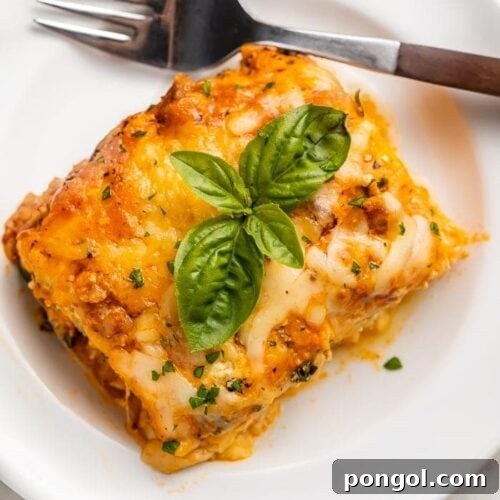 A deliciously cooked slice of keto lasagna on a white plate with a fork, ready to be eaten.