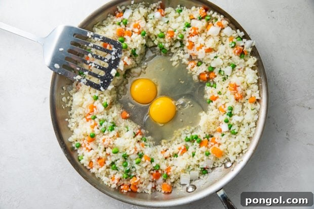 Frozen vegetables surrounding two eggs in a large wok with a spatula