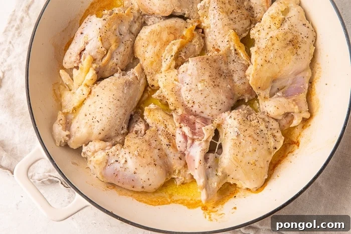 Heavy sauté pan full of chicken thighs in olive oil, browning