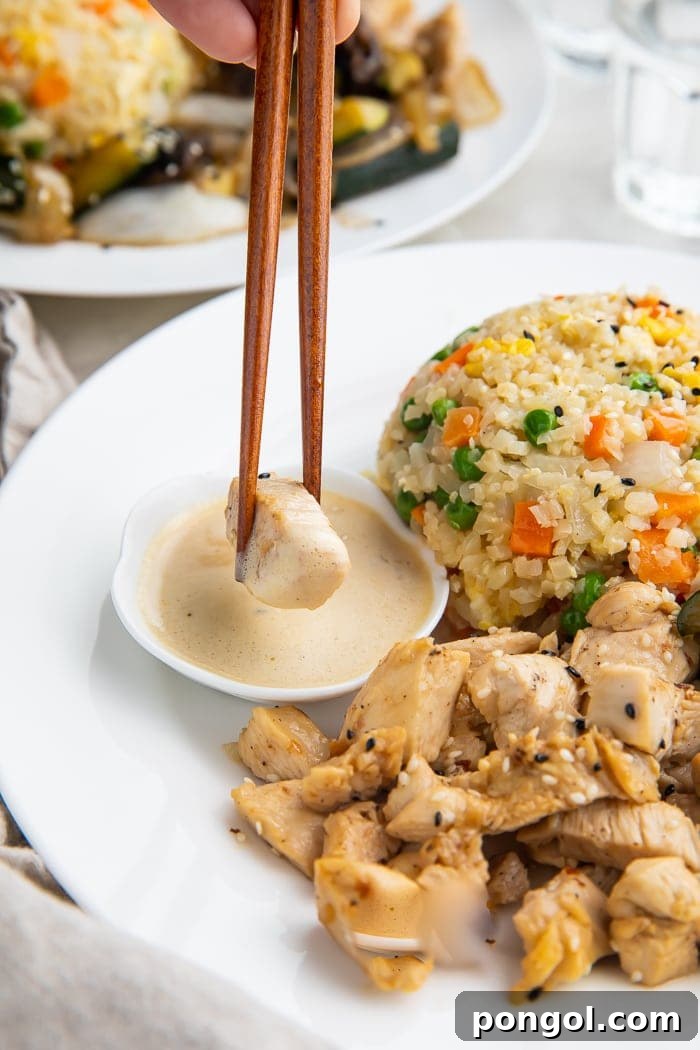 Whole30 hibachi chicken dipped in mustard sauce next to a scoop of whole30 fried cauliflower rice.