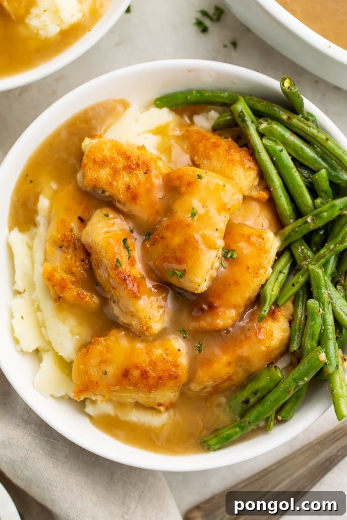 Whole30 fried chicken and gravy on a bed of mashed potatoes, served in a bowl with tender-crisp green beans.