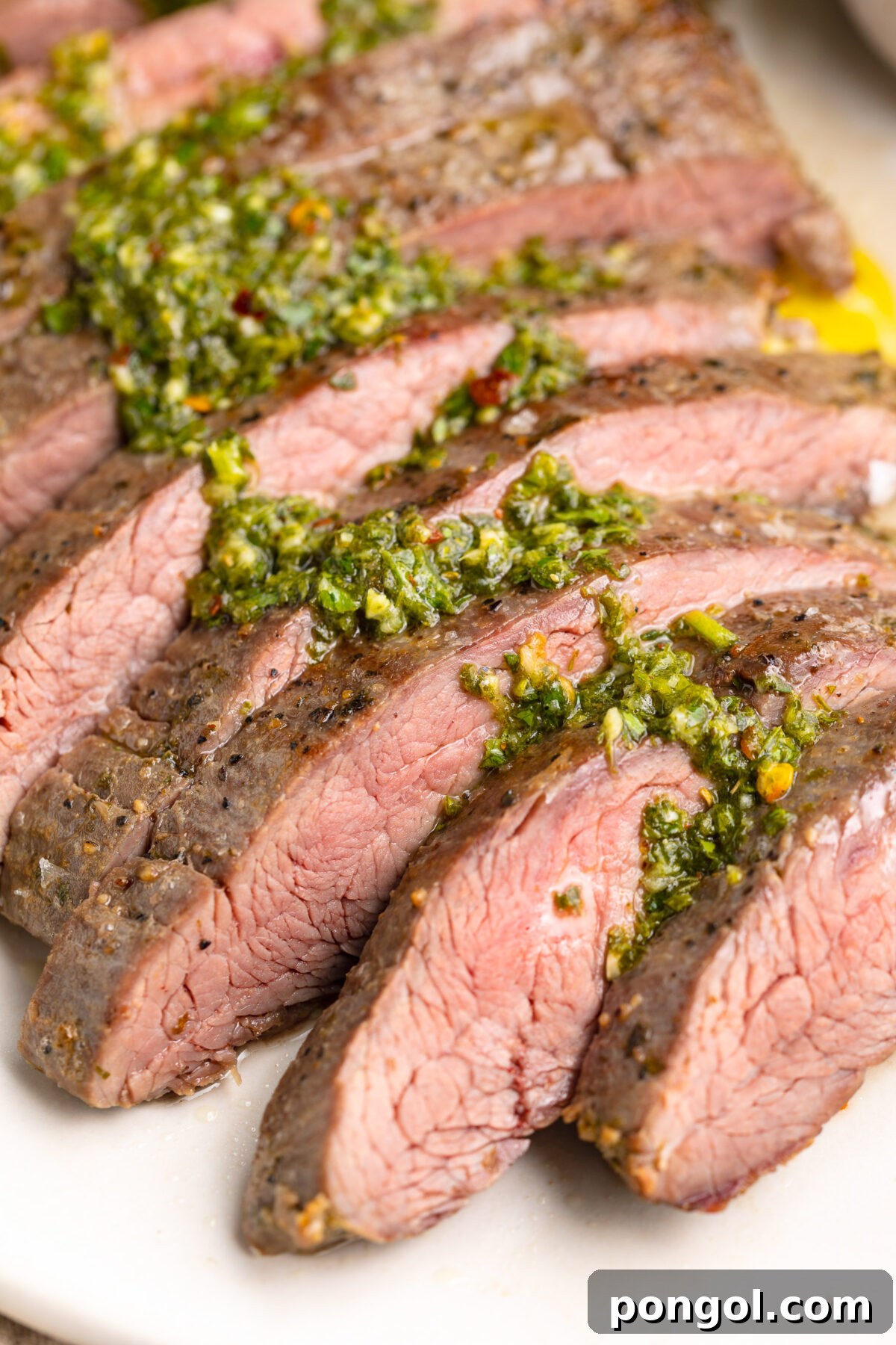 Sous vide flank steak, sliced thin and topped with green chimicuhrri resting on a platter.