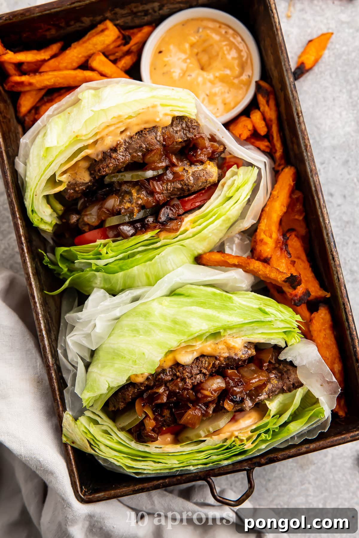 Overhead view of two Whole30 In-n-out burgers in a serving tray with sweet potato fries and animal sauce