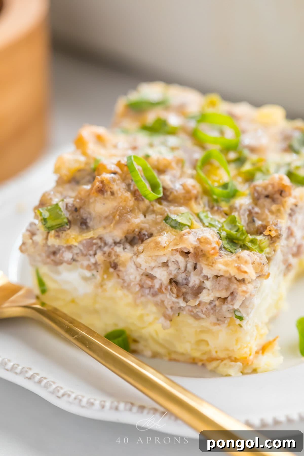 A square slice of a hashbrown breakfast casserole resting on a white plate with a gold fork.