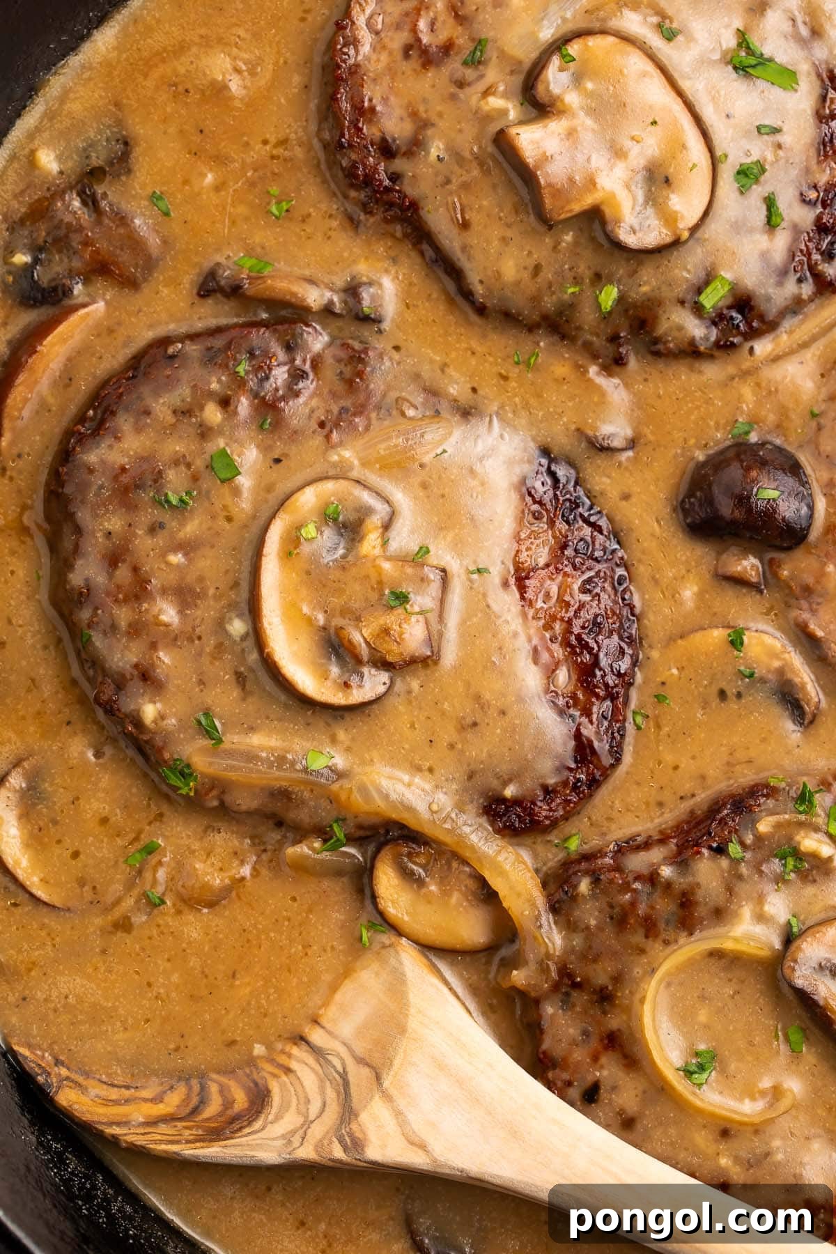 Whole30 salisbury steak in a cast-iron skillet with plenty of brown gravy, mushrooms, and a wooden spoon.