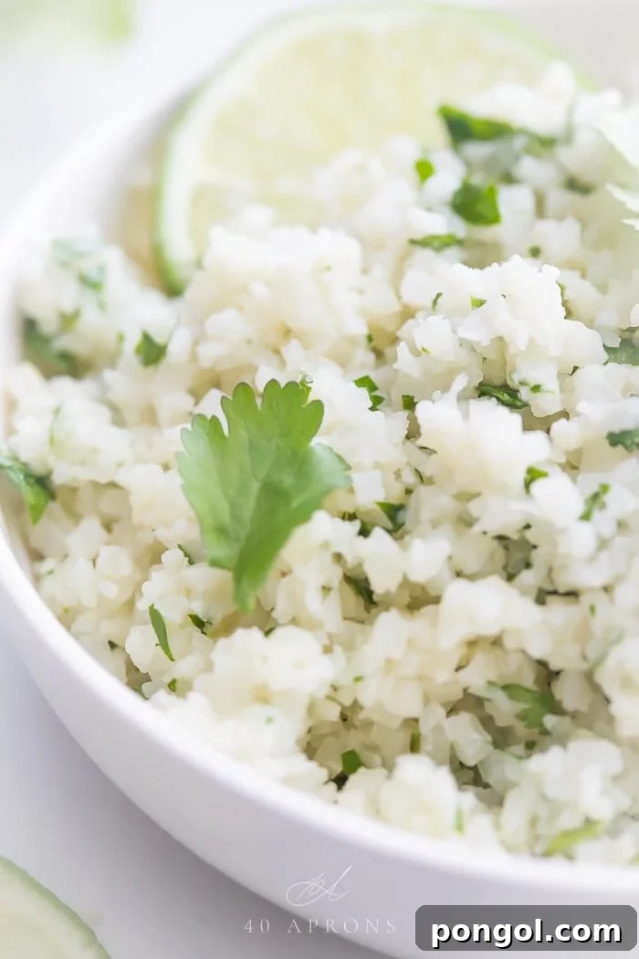 A white bowl of cilantro lime cauliflower rice with cilantro and lime garnishes.