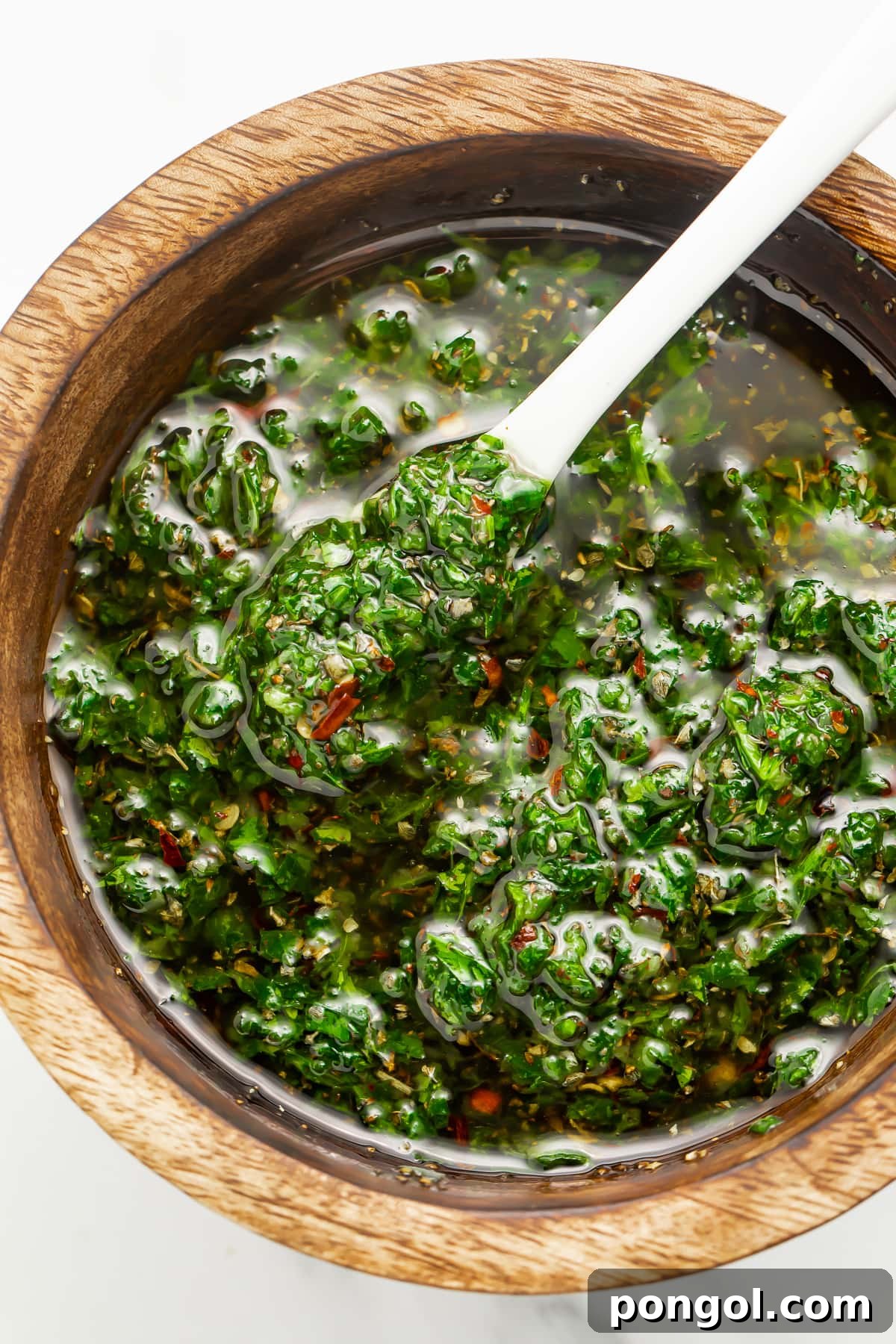 Overhead view of Texas de Brazil chimichurri sauce in a small wooden bowl with a spoon.
