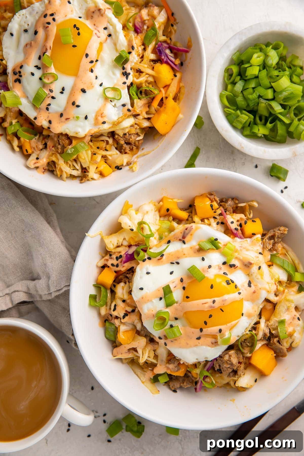 Two white bowls holding a coleslaw, mango, pork sausage mixture topped with fried eggs and green onions