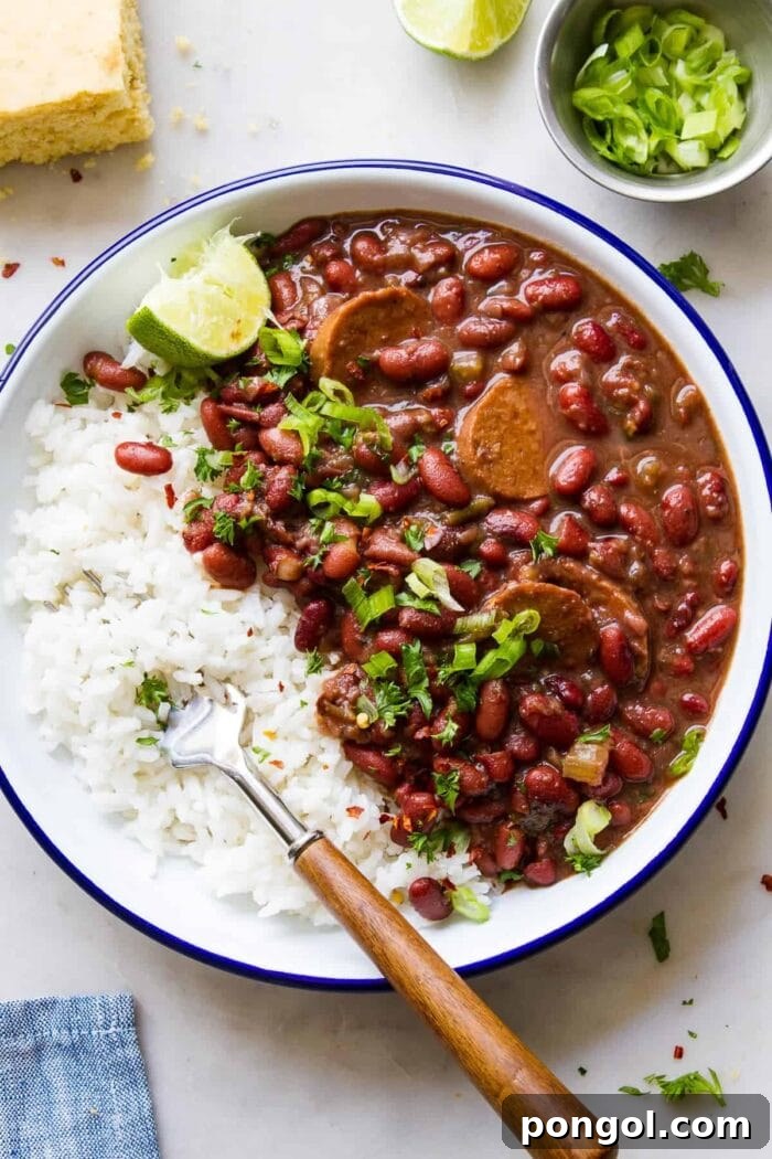 A close-up of a rustic bowl filled with red beans and vegan sausage, served alongside fluffy white rice and fresh garnish.