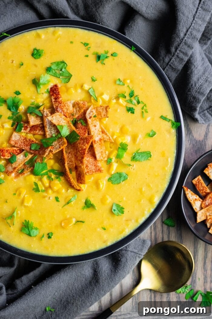 A black bowl filled with creamy yellow corn chowder, garnished with fresh herbs, offering a warm and inviting meal.