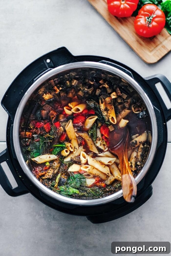 A vibrant display of marinara pasta and fresh vegetables nestled within an Instant Pot, with a wooden spoon ready for serving.