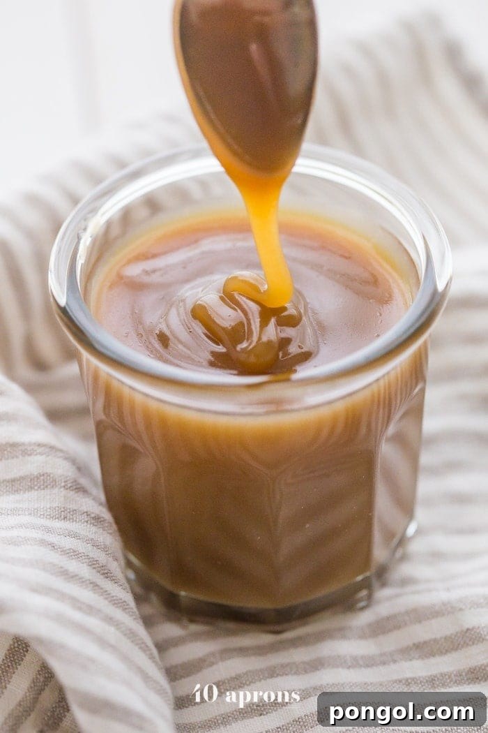 Luscious vegan Instant Pot caramel sauce gracefully drizzling off a spoon into a glass jar, promising sweet perfection.