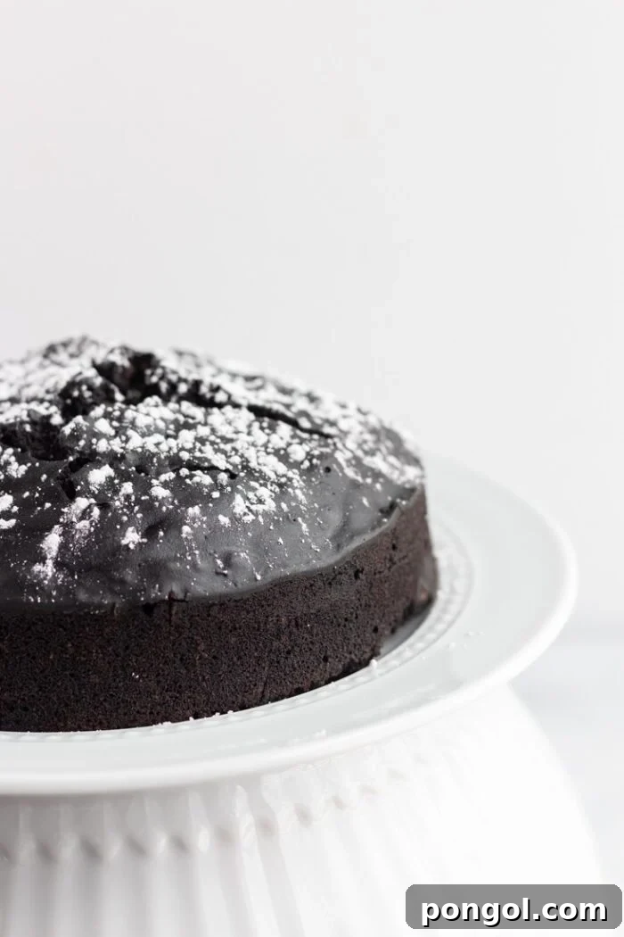 A luscious half of a vegan chocolate cake, beautifully presented on a white cake stand against a soft white background.