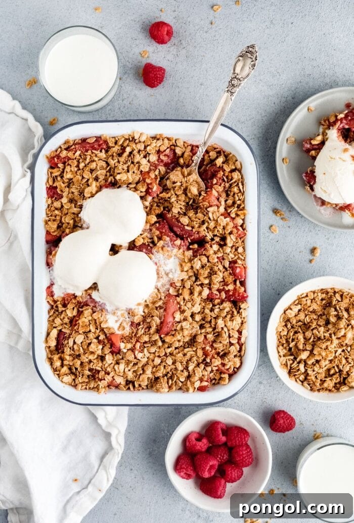 A charming casserole dish brimming with warm peach berry crisp, generously topped with a scoop of creamy vegan ice cream.