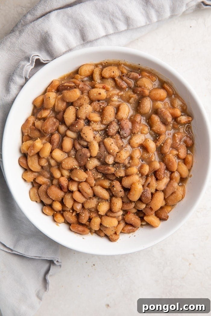 An overhead view of a white bowl filled with perfectly cooked vegan Instant Pot pinto beans, set on a elegant marble countertop.