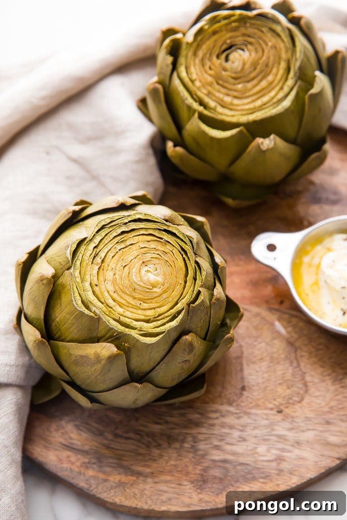 Two beautifully cooked Instant Pot artichokes presented on a rustic wooden cutting tray, accompanied by dipping sauce and a napkin.