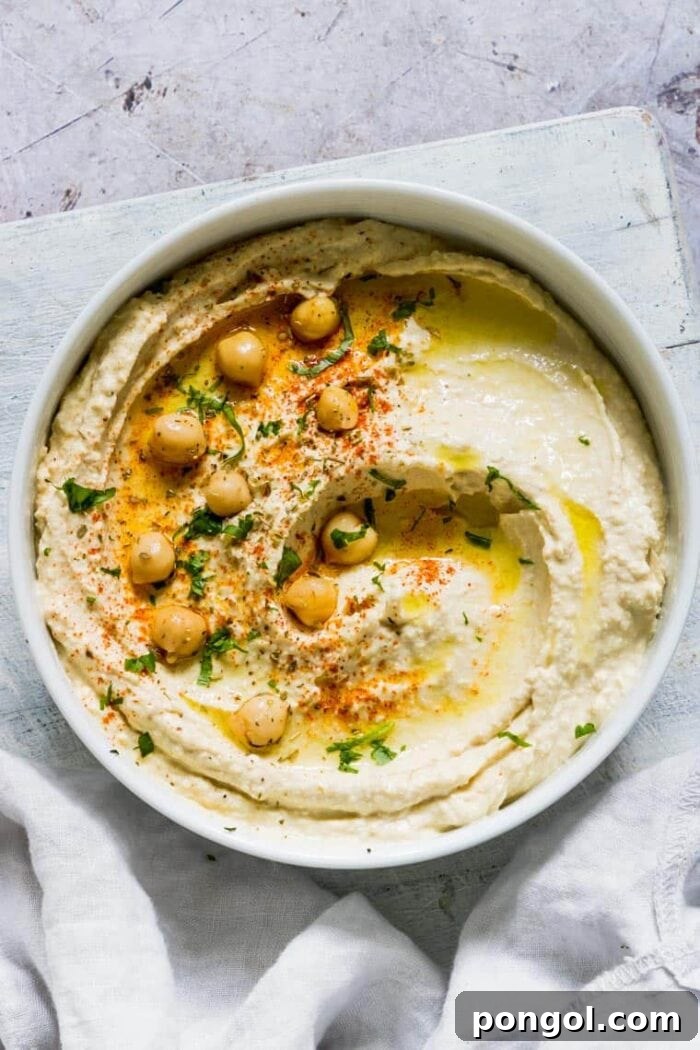 An inviting overhead photo of a creamy bowl of vegan Instant Pot hummus, garnished with whole chickpeas and a drizzle of olive oil.