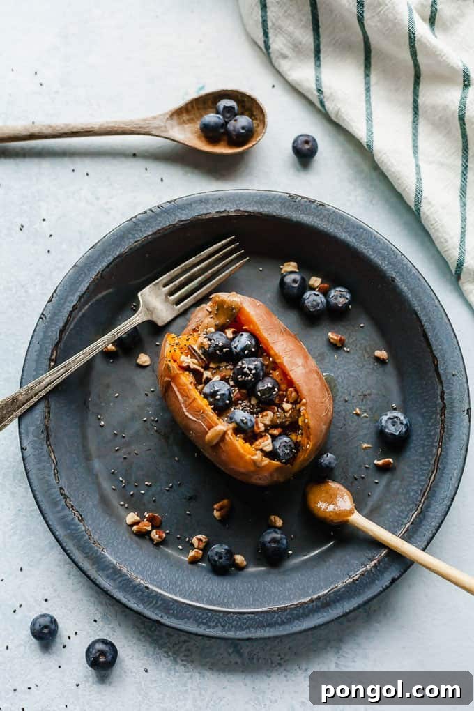 A beautifully plated breakfast stuffed sweet potato on a grey-blue dish, accompanied by a fork and scattered fresh blueberries.