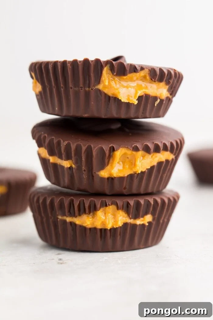 Decadent Keto Peanut Butter Cups 7 A close-up, zoomed out view of three perfectly stacked keto peanut butter cups on a minimalistic white background, emphasizing their pristine appearance and inviting texture.