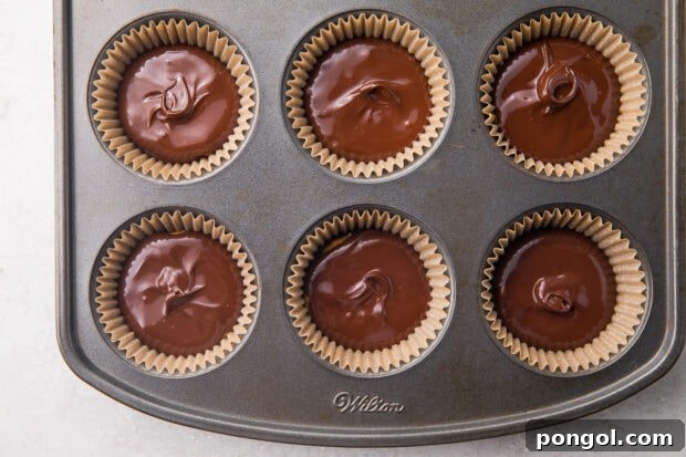 Finished keto peanut butter cups in a cupcake pan, showcasing their smooth, even top chocolate layer, ready for chilling.