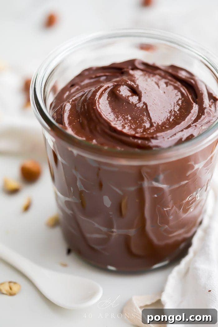A beautifully presented jar of homemade vegan Nutella, surrounded by whole and shelled hazelnuts, suggesting freshness and natural ingredients. The focus is on the rich, creamy texture and vibrant color of the chocolate hazelnut spread.