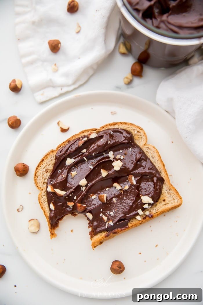 A perfectly toasted slice of bread, generously coated with homemade vegan Nutella, with a bite taken out to reveal its creamy texture. The focus is on the delicious application of the spread, making it irresistible.
