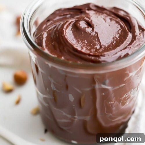 A jar of vegan Nutella with hazelnuts in the background