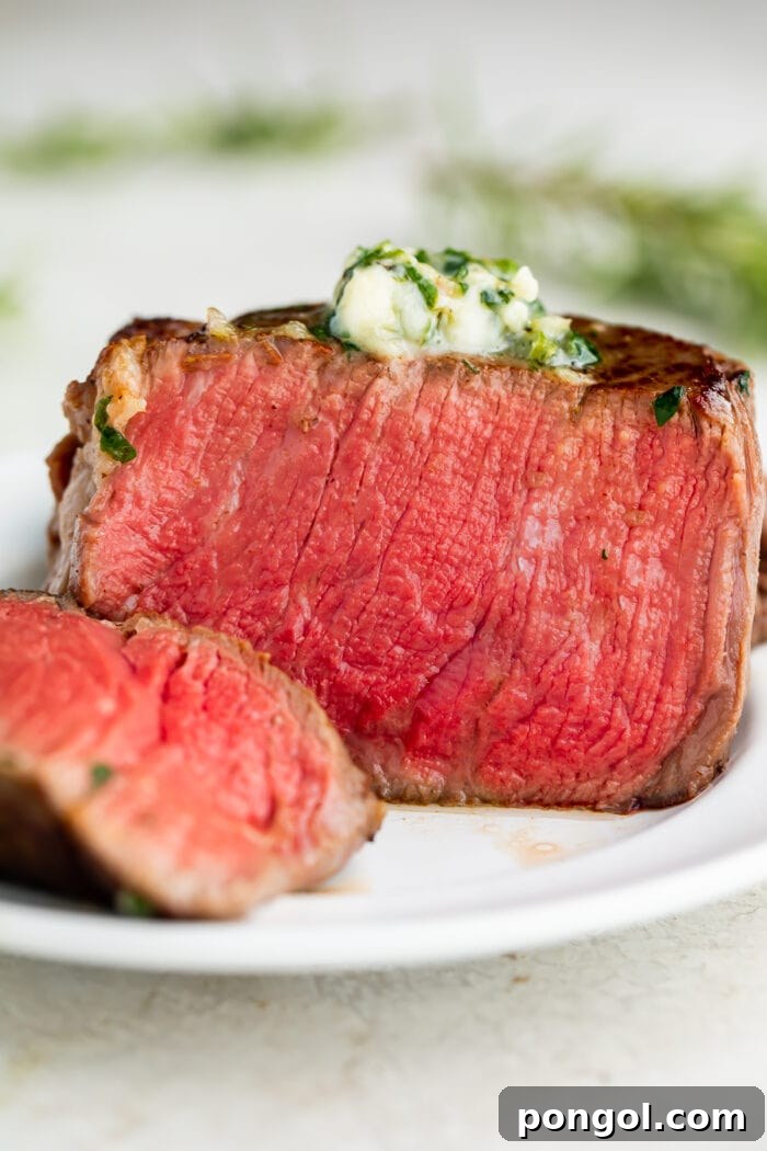 A perfectly cooked sous vide filet mignon, medium-rare, served on a white plate, topped with melting herb butter.