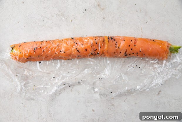 The completed salmon roll, meticulously wrapped in plastic and ready for the crucial refrigeration step to firm up