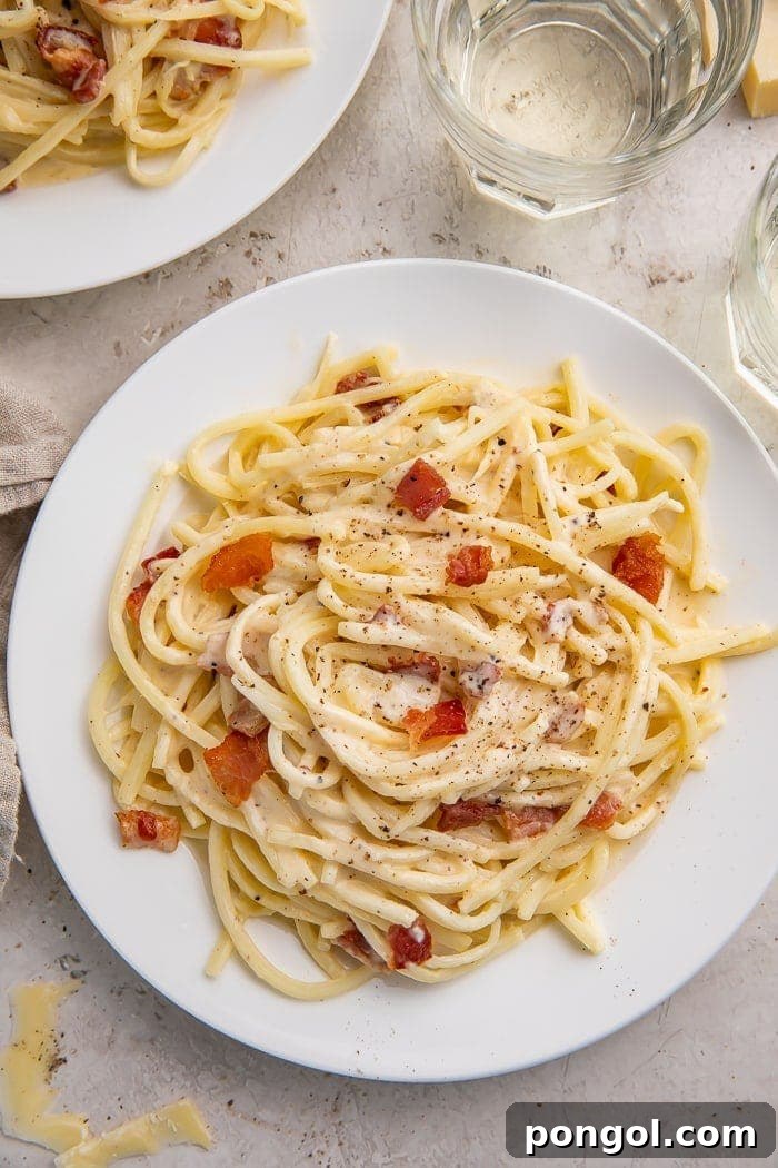 A full white plate of keto carbonara on a white tablecloth next to a glass of water
