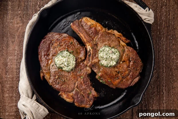 Two perfectly seared ribeye steaks, glistening with butter, in a hot cast-iron skillet.