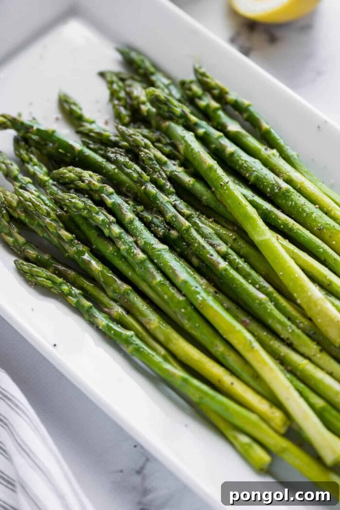A white platter generously holding perfectly cooked asparagus stalks, ready to be served
