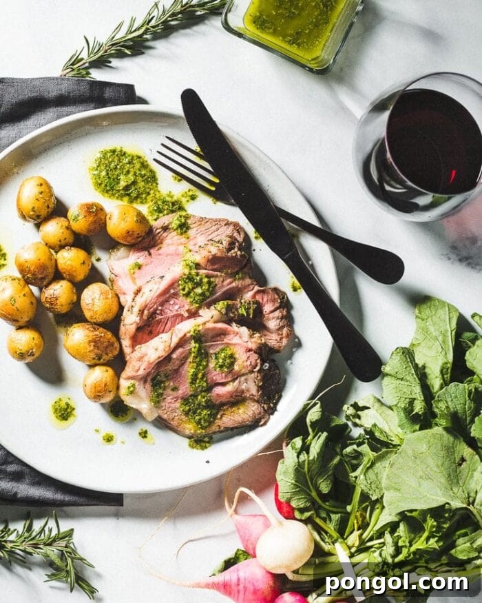 Plated leg of lamb, herb-crusted and served with roasted potatoes, fresh lettuce, and elegant black silverware