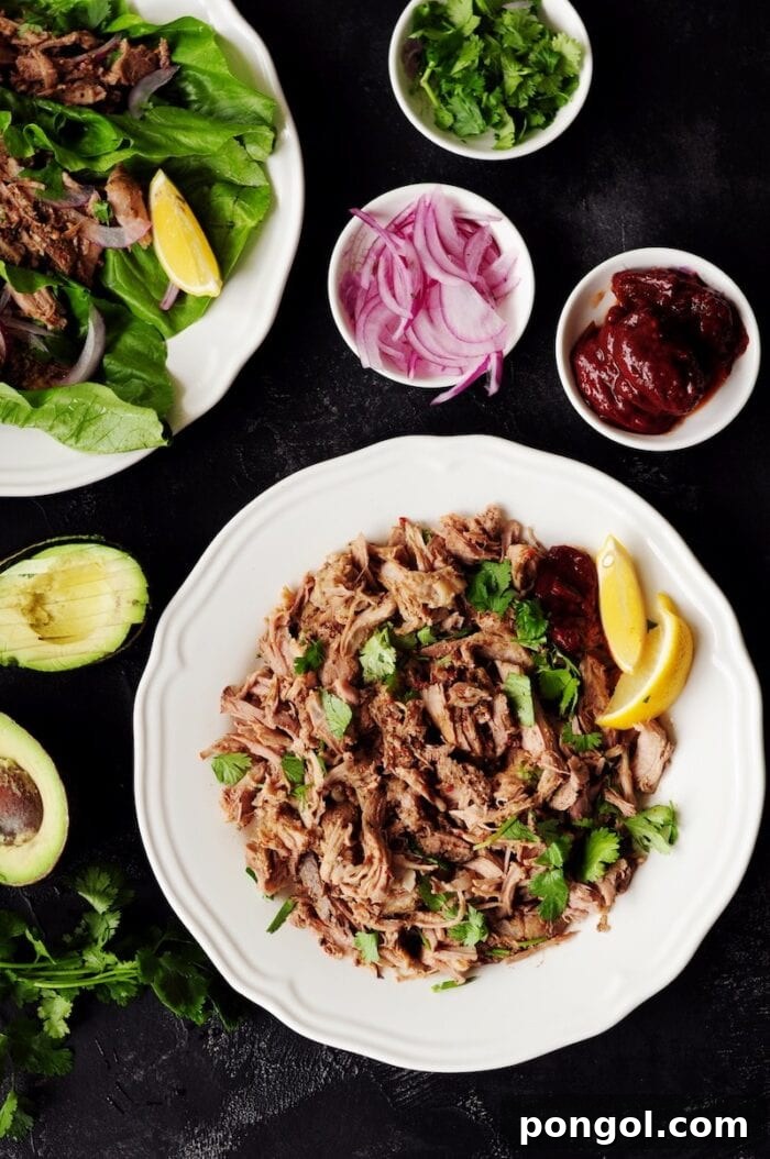 Sous vide Mexican pulled pork in a white bowl, accompanied by smaller bowls of fresh garnishes for Mexican street tacos