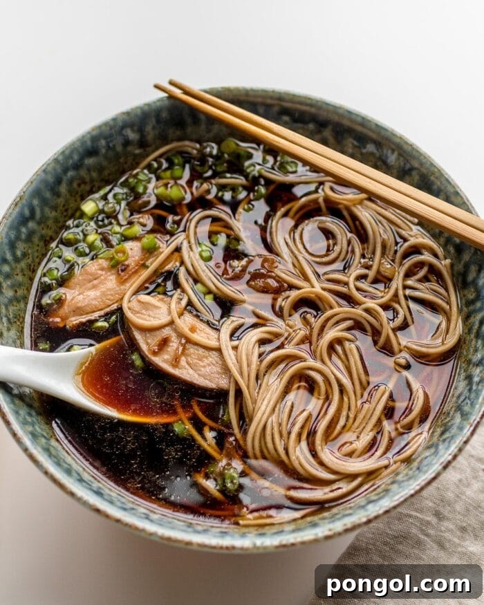 A hearty bowl of Japanese sous-vide duck ramen, complete with duck slices, broth, and garnishes, served with a spoon and chopsticks