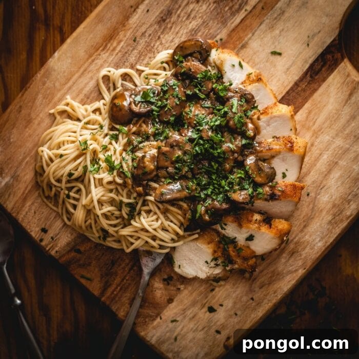 Closeup of pasta, perfectly cooked chicken marsala, and earthy mushrooms served on a rustic cutting board