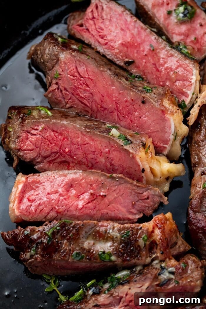 Red interior of a medium-rare cut sous vide ribeye arranged on a plate, garnished with fresh herbs and a pat of rich compound butter.