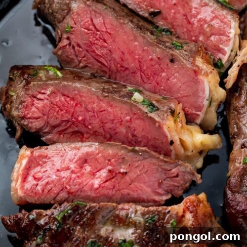 Red interior of a medium-rare cut sous vide ribeye arranged on a plate with compound butter and fresh herbs.