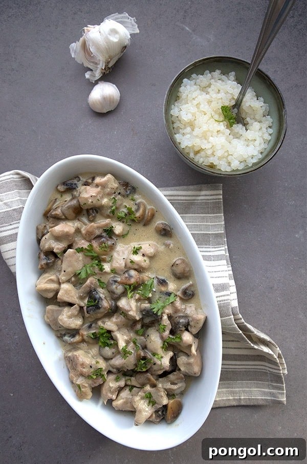 A white boat dish with chicken and mushrooms on a dark countertop