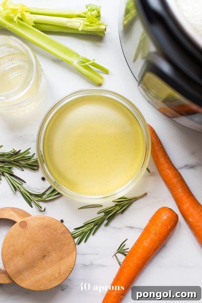 A mason jar of bone broth next to an Instant Pot on a grey countertop. Celery and carrots are scattered around.