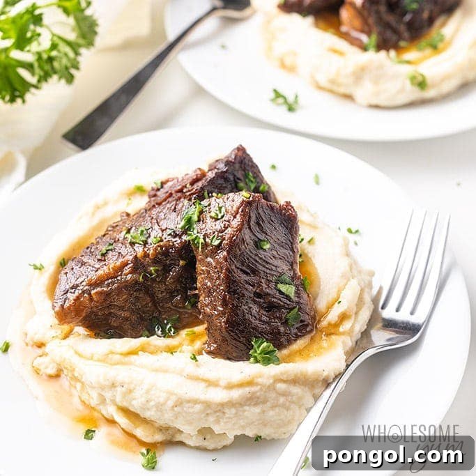 Beef short ribs on top of mashed potatoes on a white plate