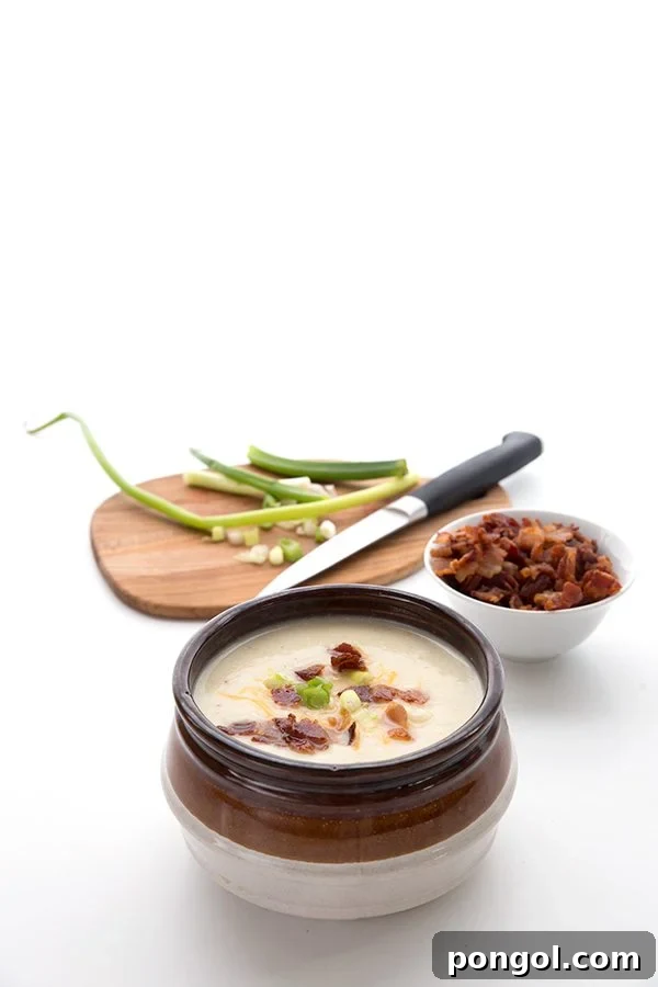 Bowl of cauliflower soup in front of bowls of garnish against a white backdrop