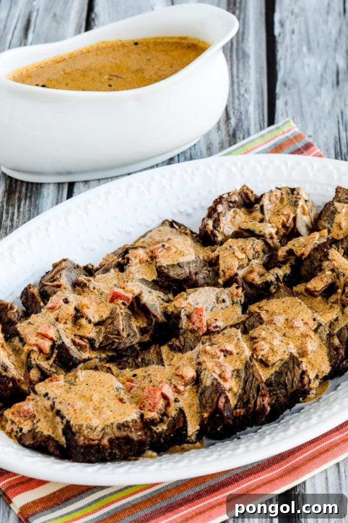 A white plate holding Hungarian pot roast in front of a white gravy boat