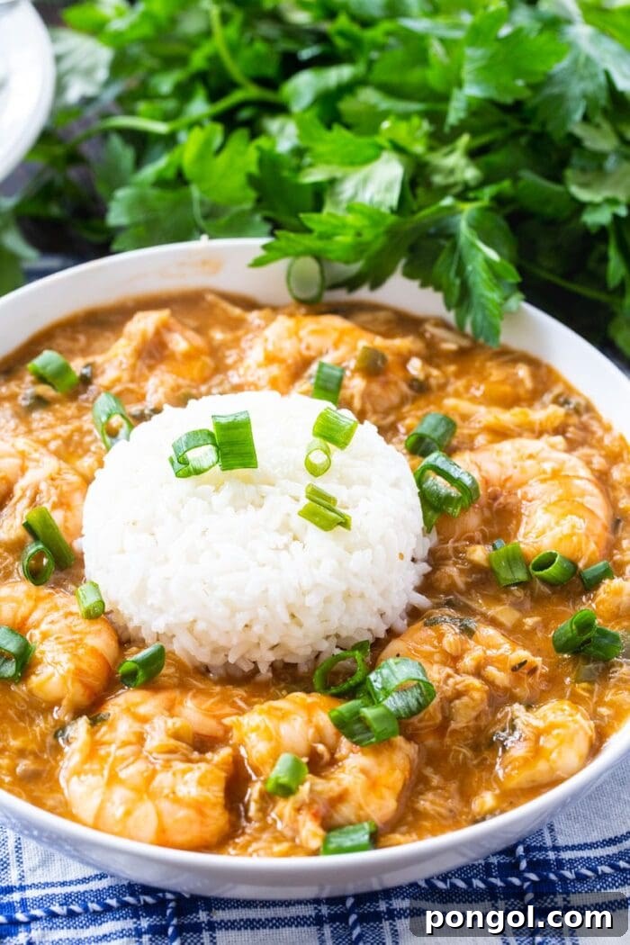 Crab and shrimp etouffee with white rice and fresh green parsley garnish, served in a rustic bowl.