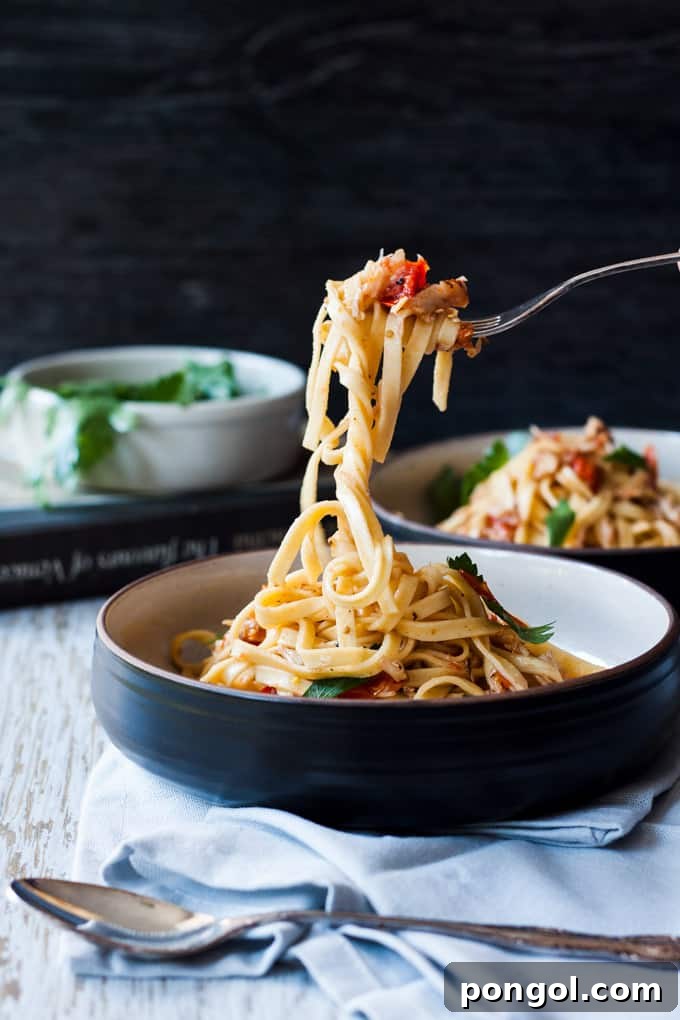 Venetian crab linguine twirled around a fork, held above a dark bowl with a white interior, showcasing its delicate strands.