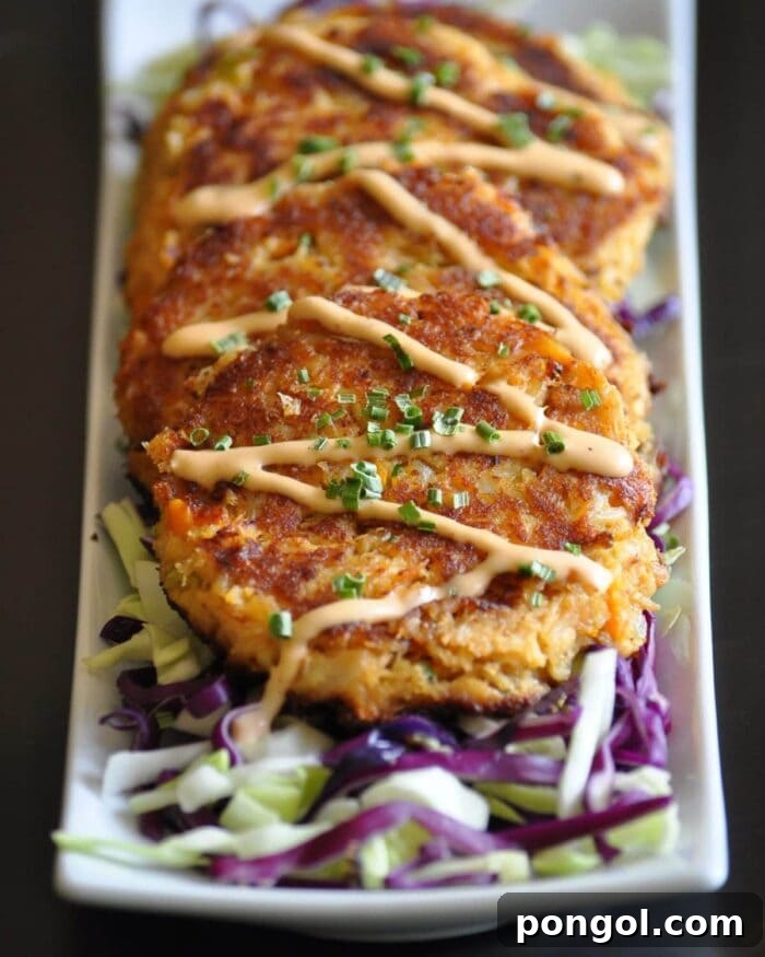 Crispy Cajun crab cakes, topped with a vibrant remoulade sauce, neatly lined on a square white platter.