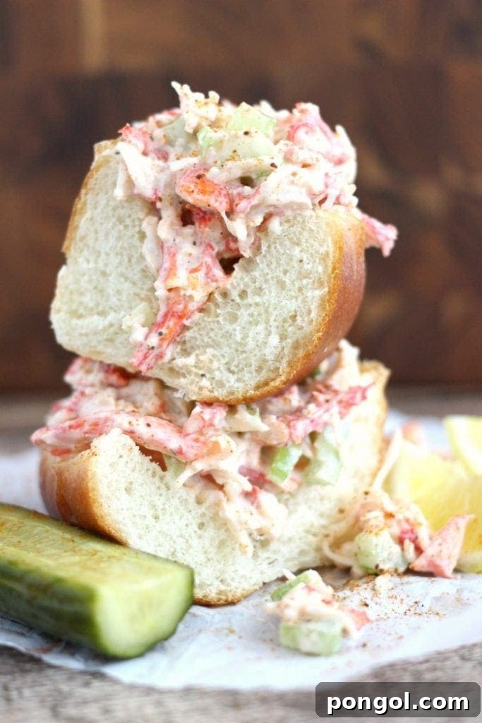 Two halves of a generous crab po'boy sandwich, one stacked atop the other, with a dill pickle spear on the side.