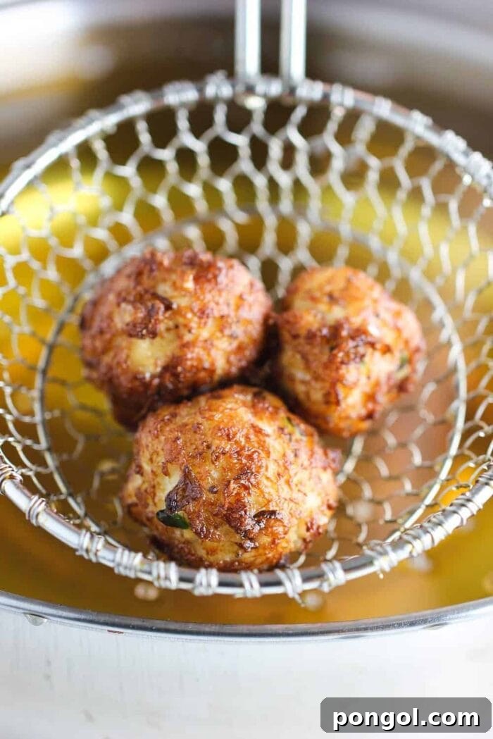 Three golden-fried beignet balls in a fry basket, being held over a pot of hot frying oil.